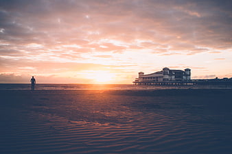 Silhouette of Man Standing on Beach at Sunset with Pier