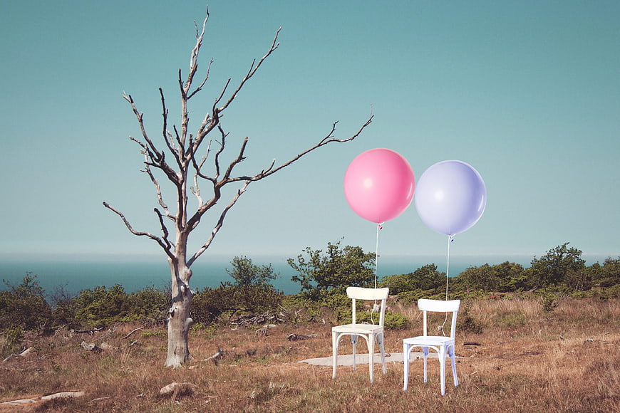 Two white chairs with pink and blue balloons in a dry landscape