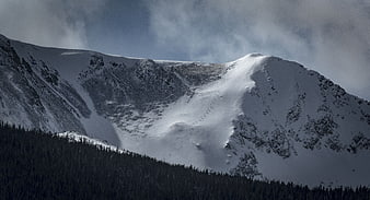 Snow-Covered Mountain Peak with Dark Forest and Cloudy Sky