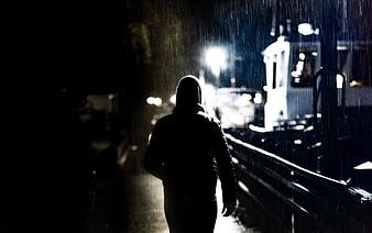 Silhouette of hooded man walking in rain at night