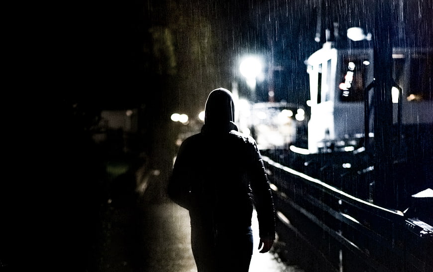 Silhouette of hooded man walking in rain at night