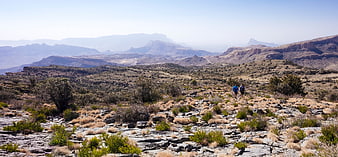 Hikers walking through rocky desert landscape with distant mountains