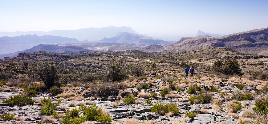 Hikers walking through rocky desert landscape with distant mountains