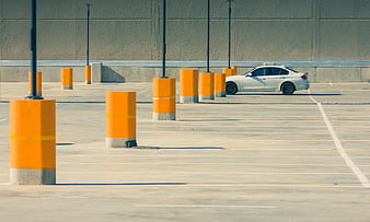 White car parked in empty lot with orange bollards