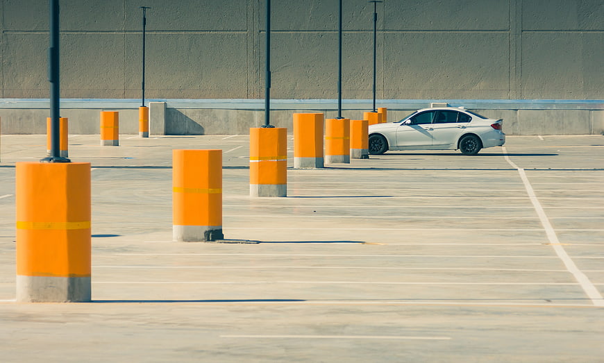 White car parked in empty lot with orange bollards