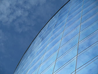 Curved Glass Building Facade Reflecting Blue Sky and Clouds