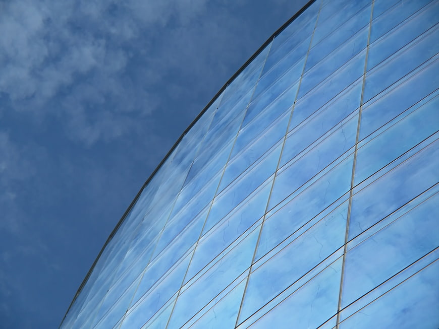 Curved Glass Building Facade Reflecting Blue Sky and Clouds