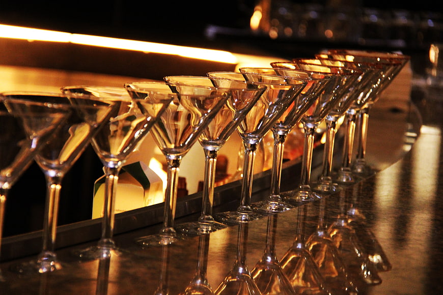 Row of empty martini glasses lined up on a dark bar counter with warm lighting