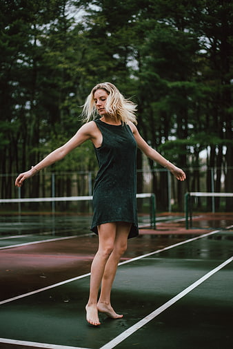 Blonde woman dancing barefoot on wet tennis court