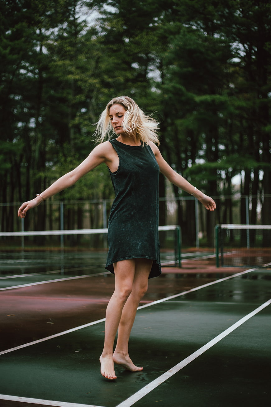 Blonde woman dancing barefoot on wet tennis court