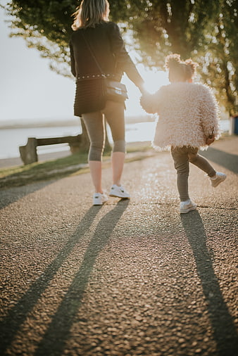 Mother and daughter walking hand in hand in golden sunlight