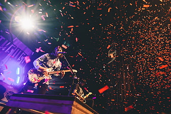 Rock musician singing and playing guitar on stage with confetti