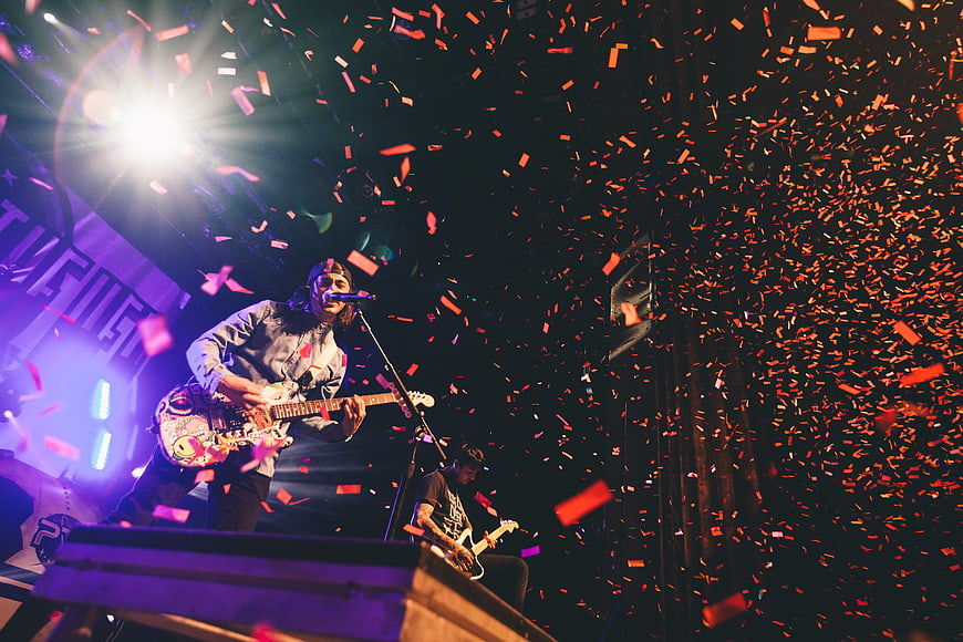 Rock musician singing and playing guitar on stage with confetti