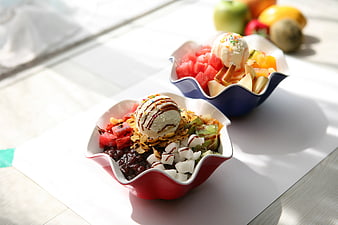 Two colorful fruit and ice cream bowls on a white table