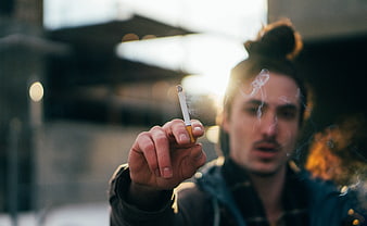 Man holding cigarette with smoke in urban setting
