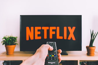 Hand holding remote control pointing at TV with Netflix logo