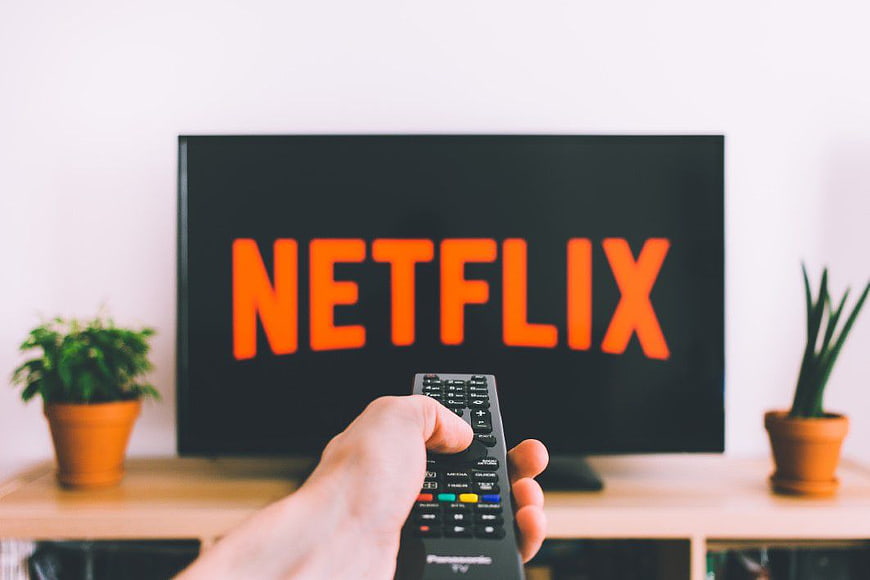Hand holding remote control pointing at TV with Netflix logo