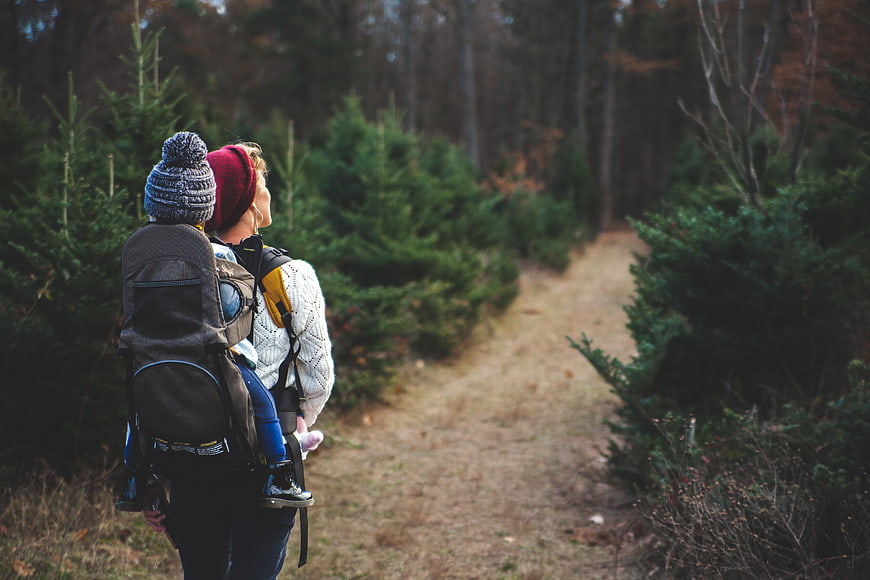 Mother hiking with baby in carrier through autumn forest