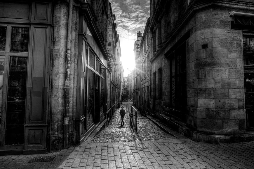 Black and white photo of a lone figure walking down a narrow cobblestone street