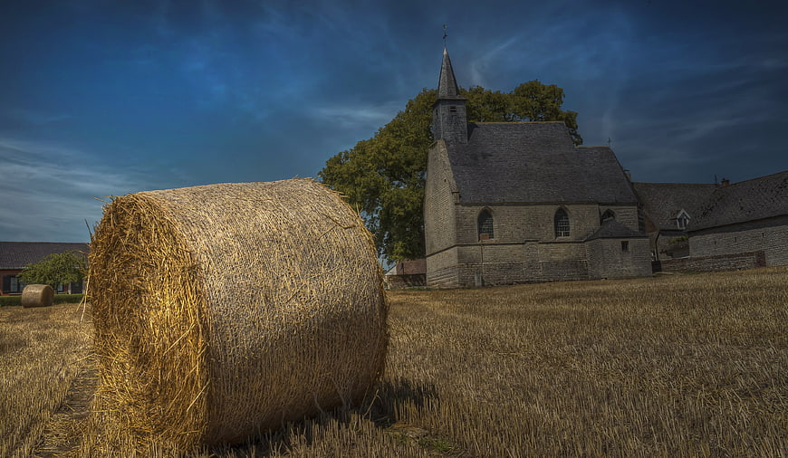 Golden Hay Bale in Harvested Field with Stone Chapel