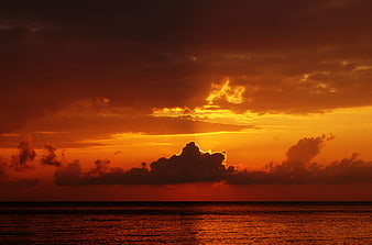 Dramatic fiery orange sunset over ocean horizon with clouds