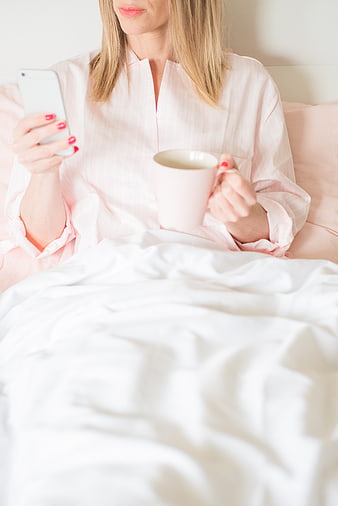 Woman in bed using smartphone with coffee cup