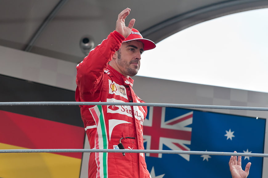 Formula 1 driver in red racing suit waving on podium