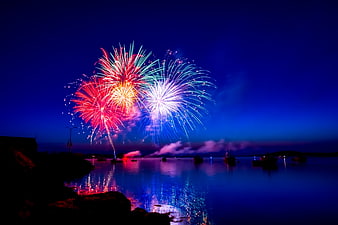 Colorful fireworks exploding over a calm harbor at night with boat silhouettes