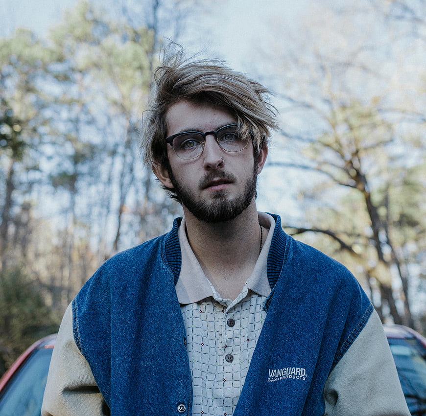 Young man with glasses and beard in varsity jacket outdoors