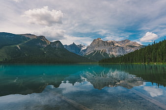 Turquoise mountain lake with forest reflection and cloudy sky