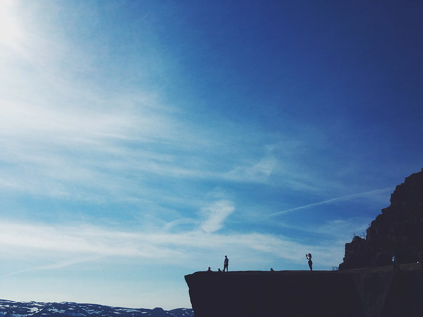 Silhouettes of People Standing on a Cliff Edge Against Blue Sky