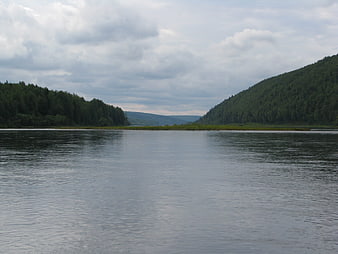 Wide River Flanked by Forested Hills Under Cloudy Sky