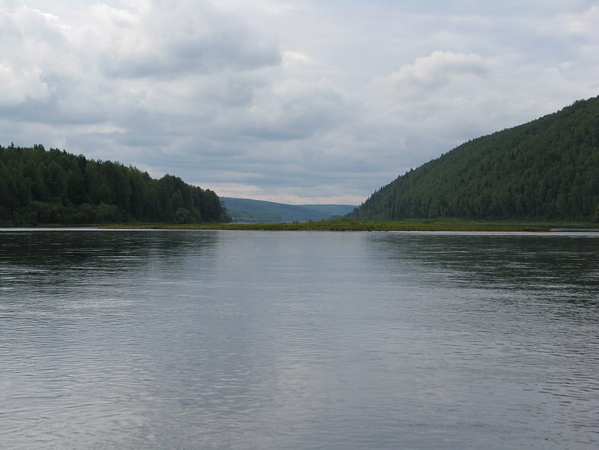 Wide River Flanked by Forested Hills Under Cloudy Sky