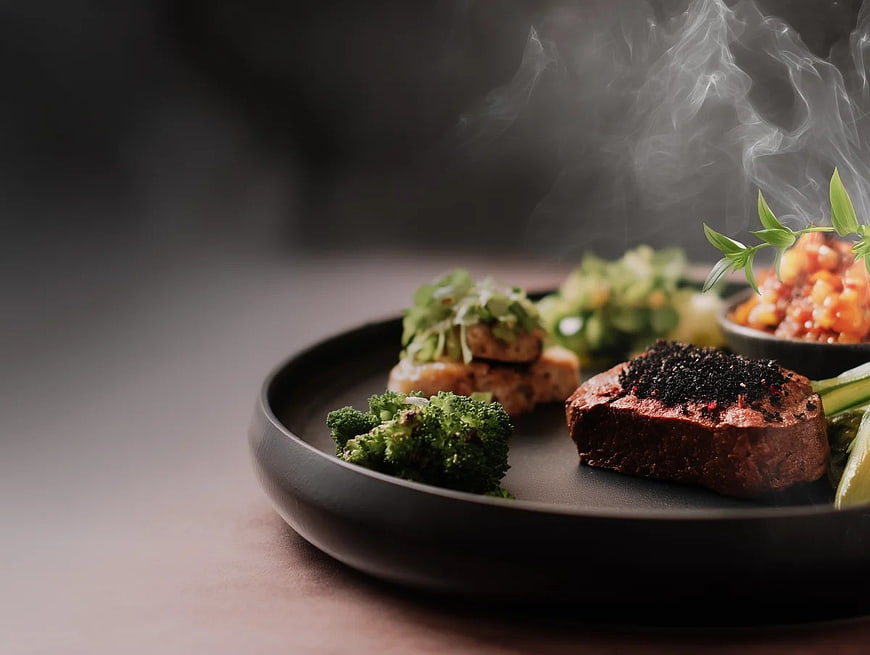 Steaming Gourmet Steak with Broccoli and Herbs on Black Plate