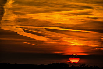 Dramatic orange sunset with streaked clouds over dark silhouette