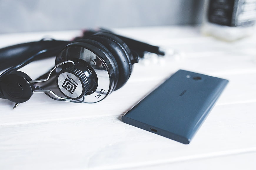 Black headphones and smartphone on white wooden table