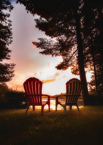 Two Adirondack Chairs Facing Lake at Sunset