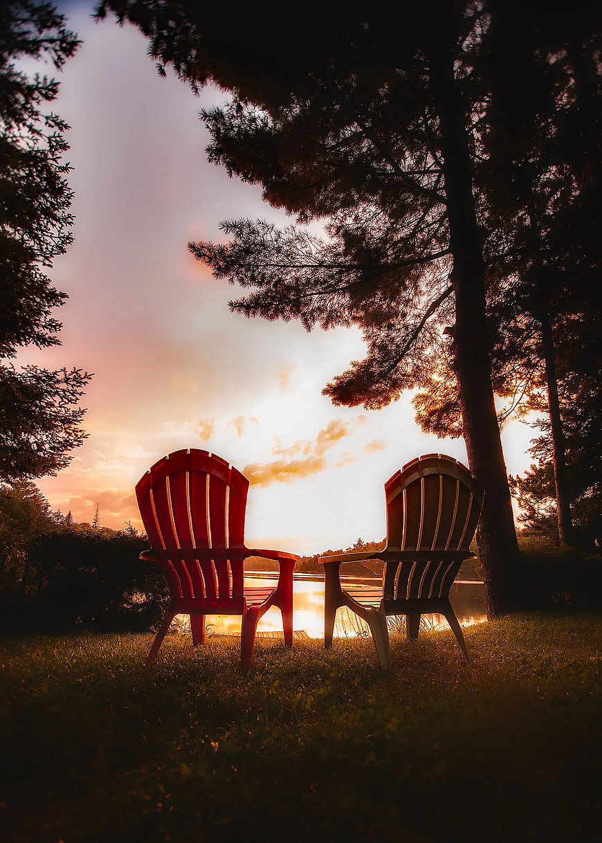 Two Adirondack Chairs Facing Lake at Sunset