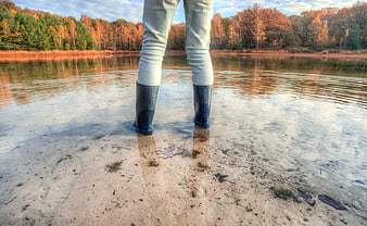 Person in rain boots standing in shallow autumn lake water