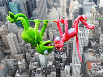 Kermit and Pink Panther plush toys hanging on a wire over a city