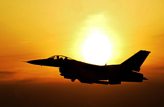Silhouette of fighter jet flying against golden sunset