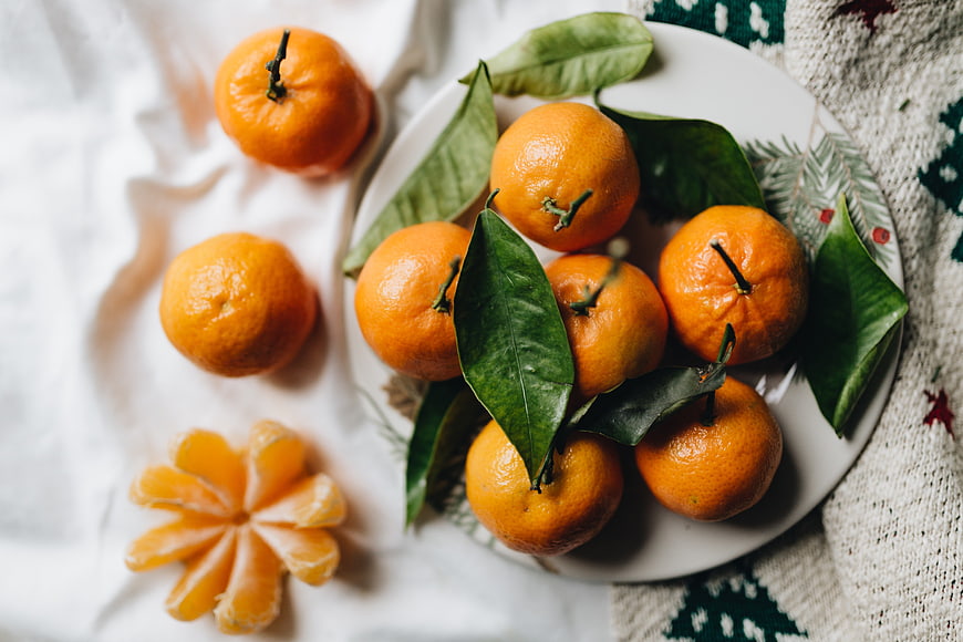 Fresh tangerines with green leaves on a white plate