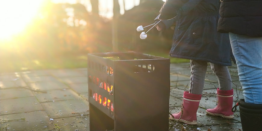 Child roasting marshmallows over outdoor fire pit at sunset
