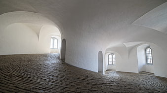 White vaulted interior with cobblestone floor and arched windows
