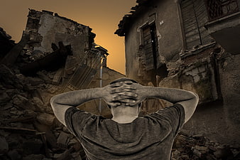 Man in despair facing destroyed buildings at sunset