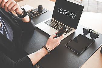 Person using smartphone and laptop with timer on desk