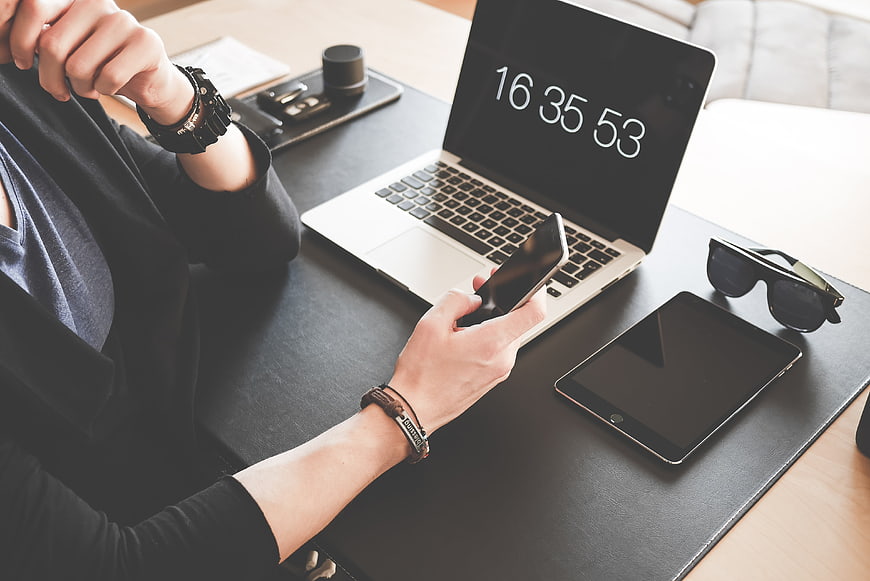 Person using smartphone and laptop with timer on desk