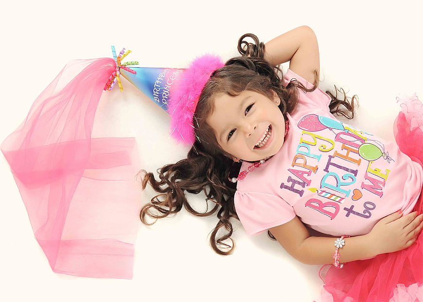 Happy little girl in pink birthday outfit lying on white background