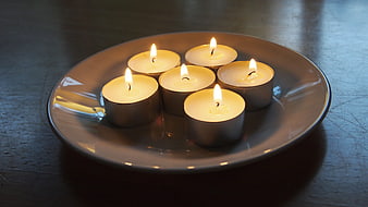 Six lit tea light candles on a ceramic plate