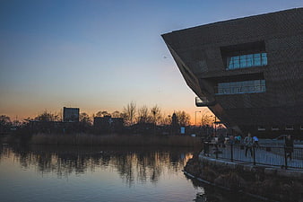 Modern angular building by river at sunset